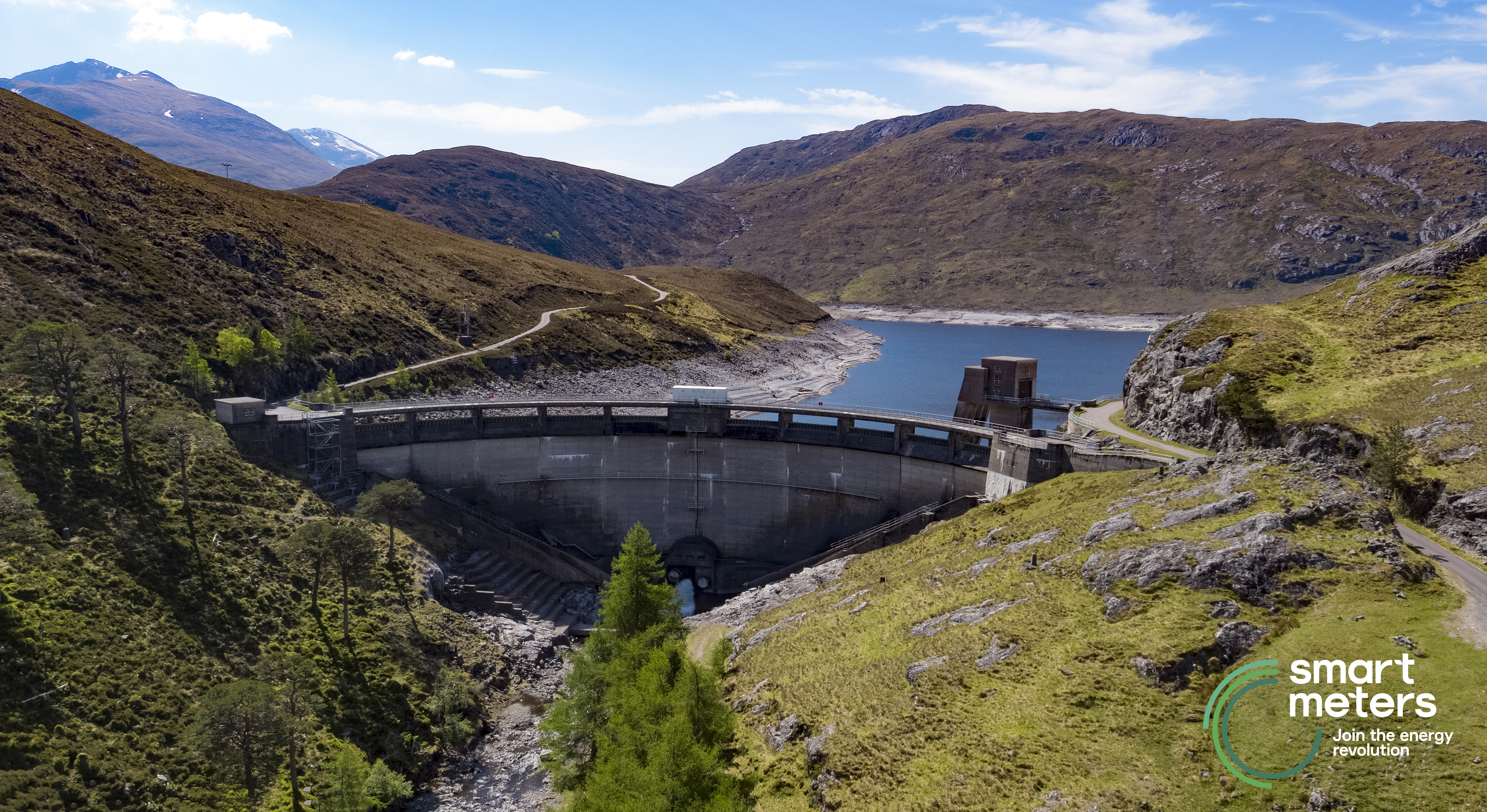 An aerial view of a hydropower dam built next to a lake in a mountainous region.